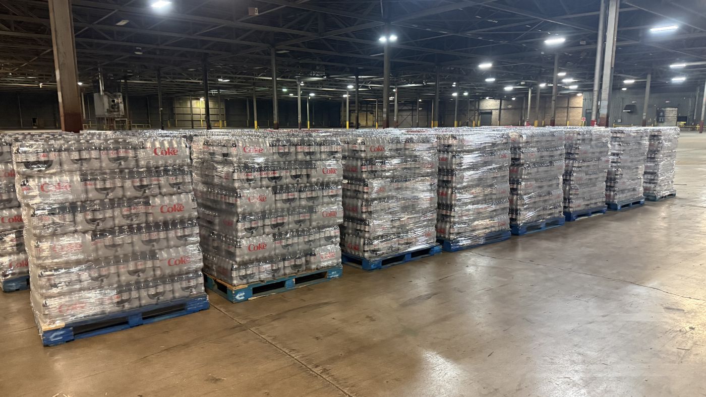 A long row of freshly restacked and shrink-wrapped beverage pallets lined up on a warehouse floor